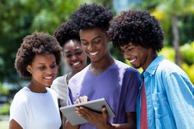 Group of african american young adults watching movie with digital tablet outdoor in the summer